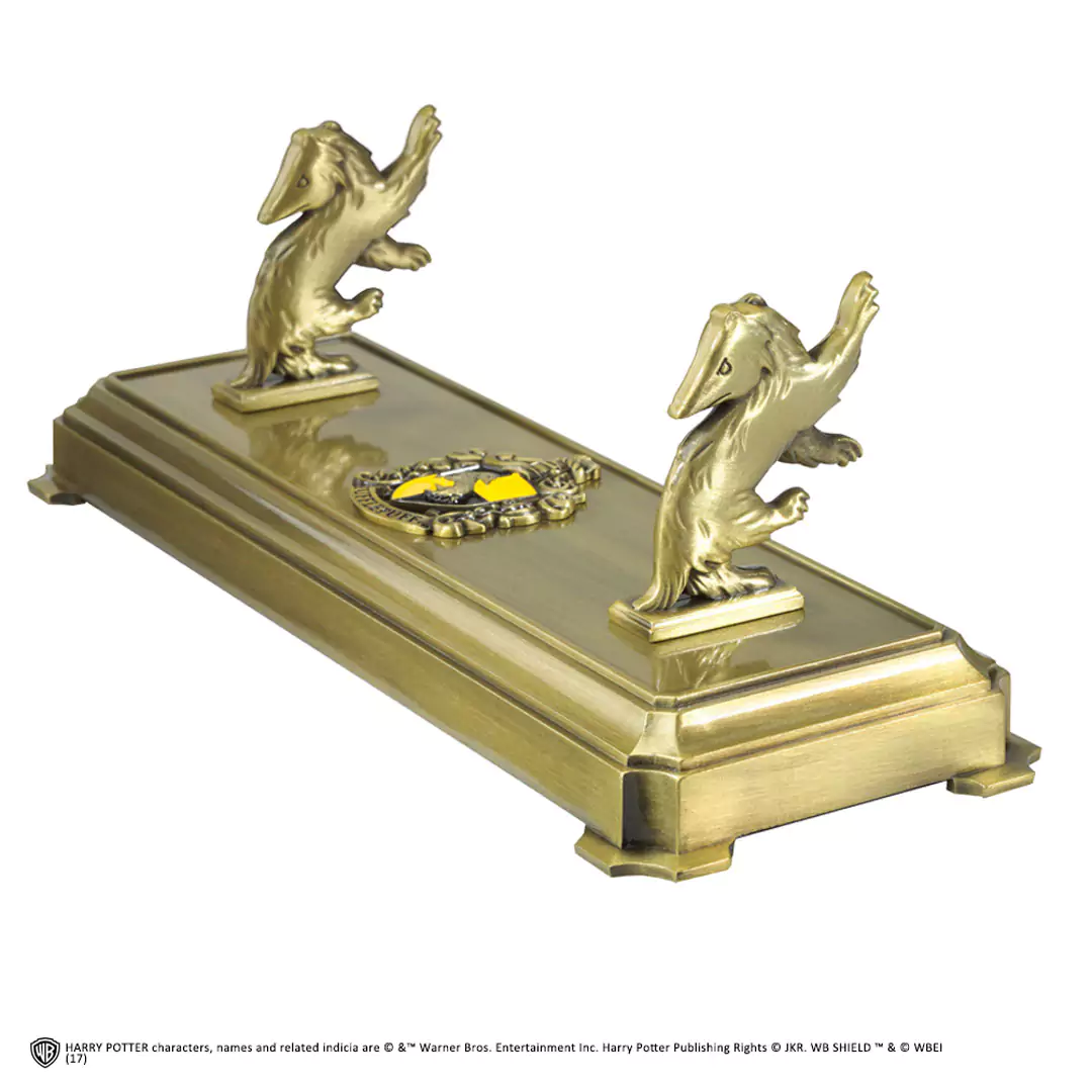 Detaillierter, offiziell lizenzierter Harry Potter Zauberstabständer im Hufflepuff-Design. Der Metallständer zeigt den Dachs und das Hufflepuff-Wappen und hält einen Zauberstab auf einem dunklen Holztisch. Ein authentisches Sammlerstück für Fans, erhältlich in unserem Kostümladen – deinem lokalen Harry Potter Shop in Berlin.