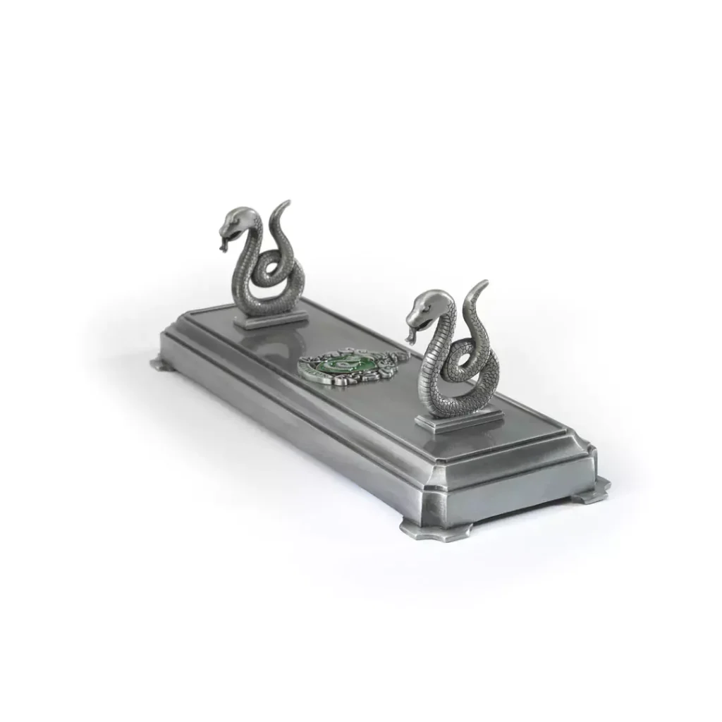 Detaillierter, offiziell lizenzierter Harry Potter Zauberstabständer im Slytherin-Design. Der Metallständer zeigt die Schlange und das Slytherin-Wappen und hält einen Zauberstab auf einem dunklen Holztisch. Ein authentisches Sammlerstück für Fans, erhältlich in unserem Kostümladen – deinem lokalen Harry Potter Shop in Berlin.