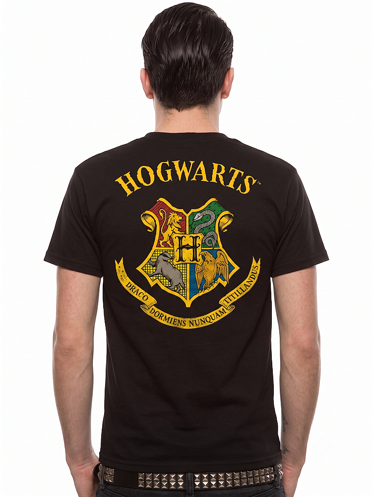 Rückenansicht eines Mannes, der ein schwarzes T-Shirt trägt. Auf dem Rücken befindet sich ein großer, farbiger Druck: Oben steht in gelben Buchstaben 'HOGWARTS'. Darunter ist das klassische Hogwarts-Wappen abgebildet, das in vier Felder für die Häuser Gryffindor (Löwe), Slytherin (Schlange), Hufflepuff (Dachs) und Ravenclaw (Adler) unterteilt ist, mit einem großen 'H' in der Mitte. Unter dem Wappen verläuft ein gelbes Banner mit dem schwarzen Schriftzug 'DRACO DORMIENS NUNQUAM TITILLANDUS'.