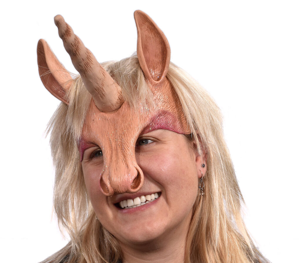 Eine fantasievolle Einhorn-Perücke mit applizierten Ohren und markanter Einhornnase, die in den Verkaufsregalen eines Berliner Maskenladens präsentiert wird.