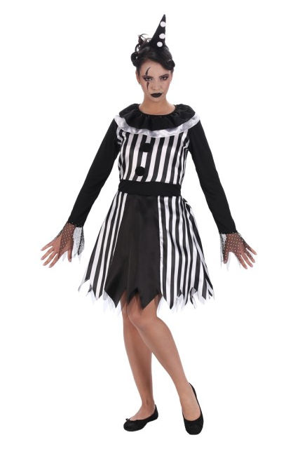 Eine Frau steht vor einem weißen Hintergrund und trägt ein schwarz-weißes Harlekin- oder Clownskostüm. Das Kostüm besteht aus einem Kleid mit einem schwarz-weiß gestreiften Oberteil, an dem zwei schwarze Pompons angebracht sind, und einem Kragen mit weißen Rüschen. Die langen, schwarzen Ärmel enden in transparenten, gepunkteten Manschetten. Der Rock des Kleides ist teils schwarz-weiß gestreift, teils einfarbig schwarz und hat einen gezackten Saum. Die Frau trägt schwarze Ballerinas, hat dunkles Make-up mit aufgemalten Tränen oder Rauten unter den Augen, schwarzen Lippenstift und trägt einen kleinen, schwarz-weiß gepunkteten Partyhut. Ihre Arme sind leicht zur Seite angewinkelt, und ihre Beine sind in einer leichten Schrittstellung positioniert.