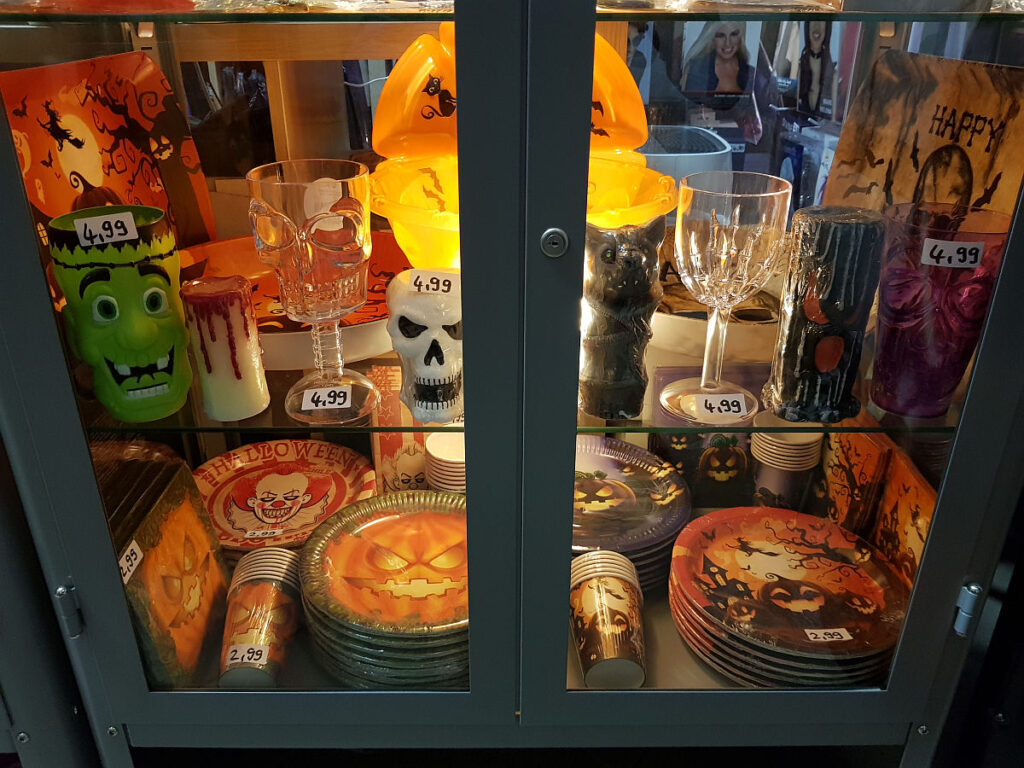 Vitrine mit gruseliger Halloween-Tischdeko und Partyzubehör. Auswahl an Papptellern, Trinkbechern, Totenkopf-Gläsern und Deko-Kerzen für die Halloween-Party im Kostümladen ClothingLand Berlin.